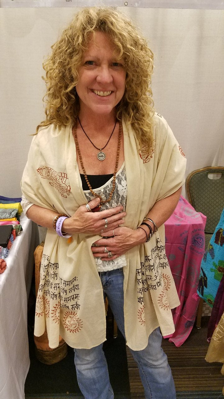 Woman wearing a beige embroidered cardigan over a patterned top, standing in front of a table with colorful items.