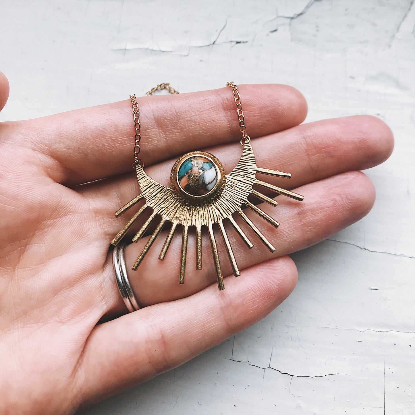 Gold necklace with a sunburst design held in a hand on a light background