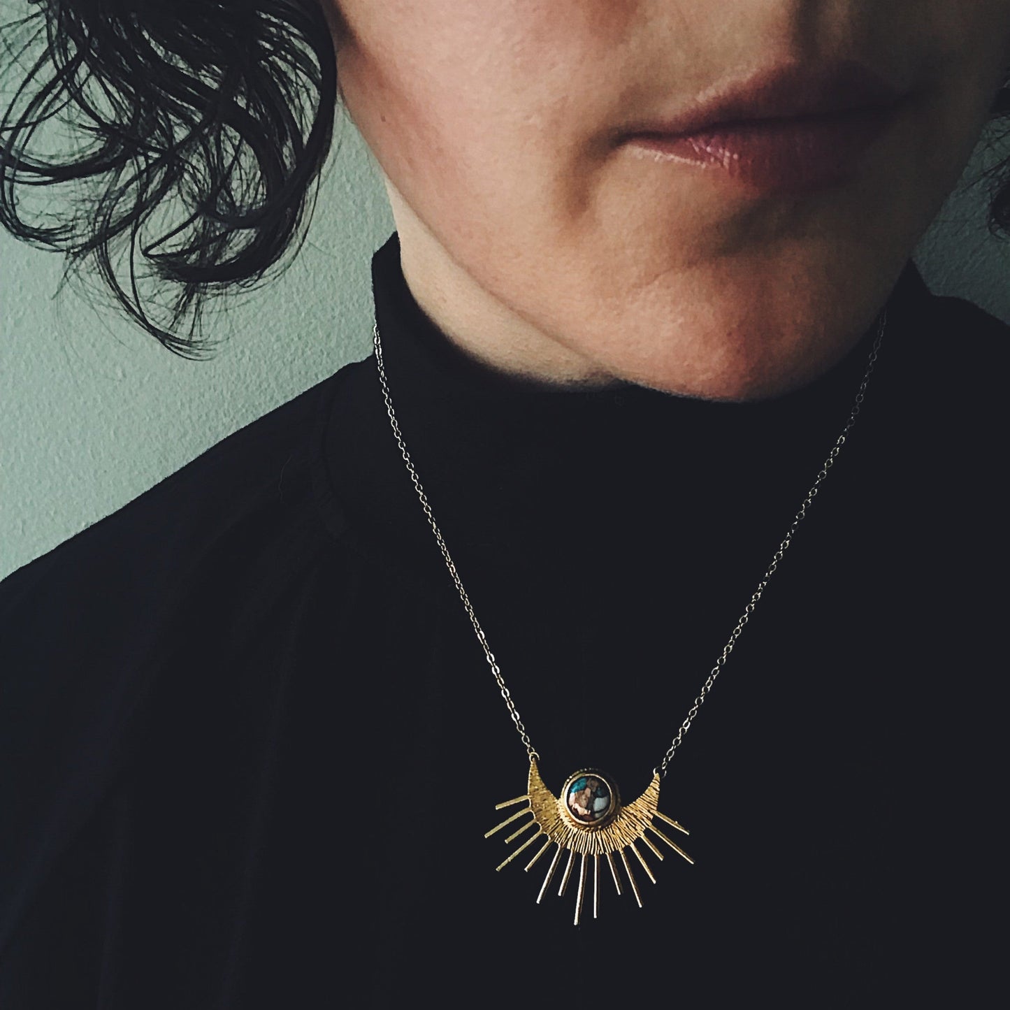 Person wearing a necklace with a sun and moon pendant against a green background