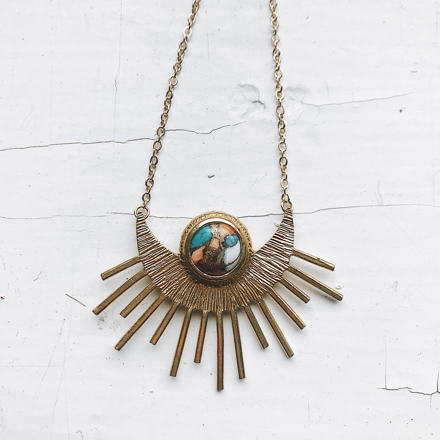 Brass sunburst necklace with a central pendant on a white textured background