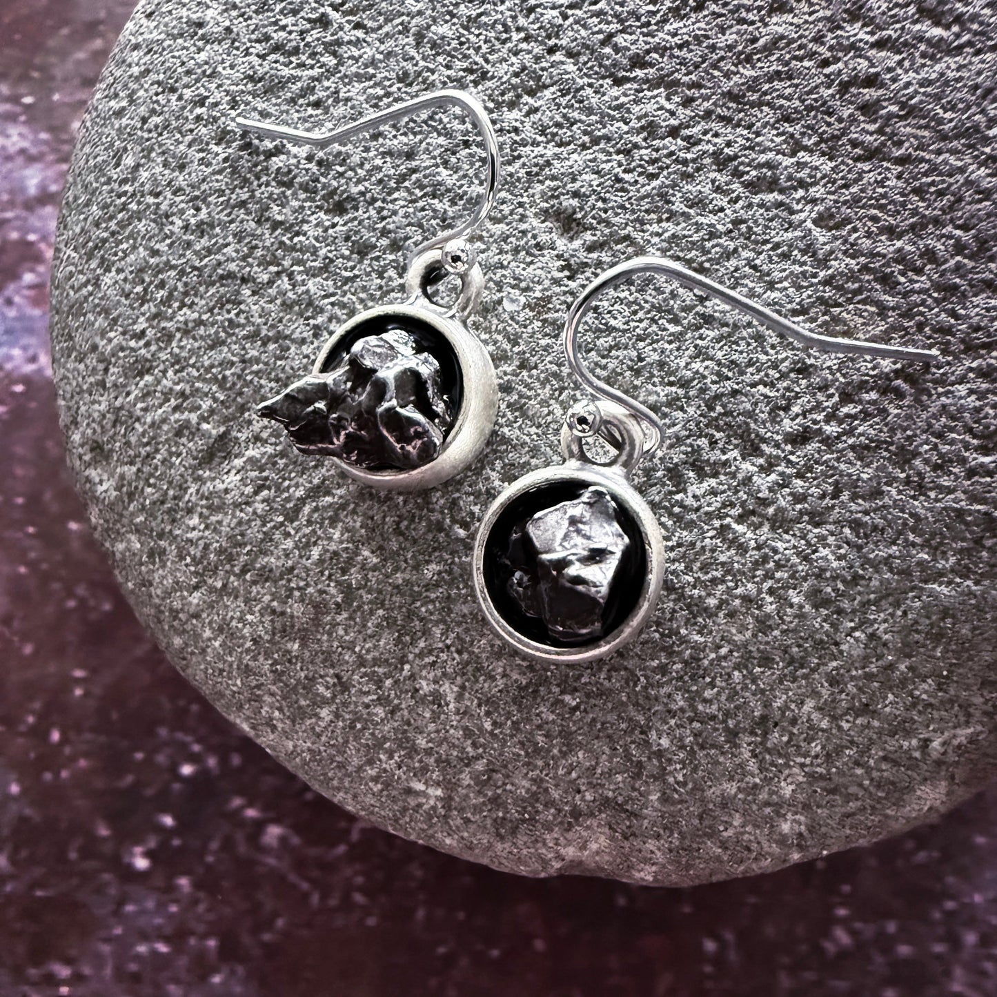 Silver earrings with dark gemstones on a textured stone surface