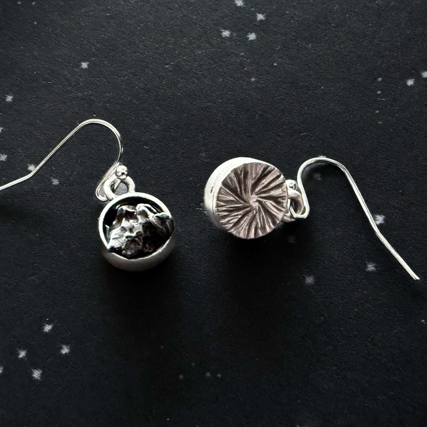 Two silver earrings on a black background