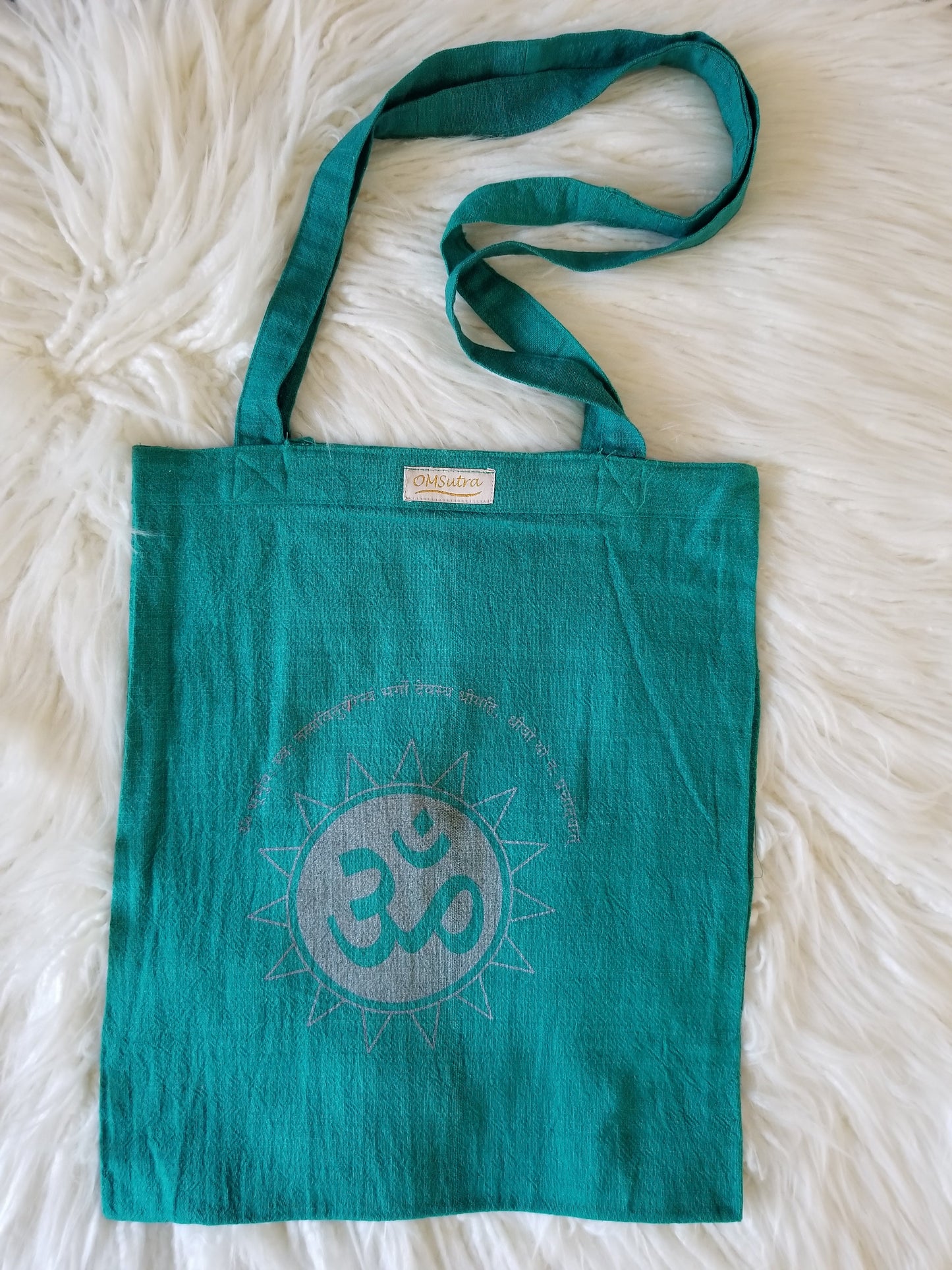 Teal tote bag with Om symbol on a white fluffy surface