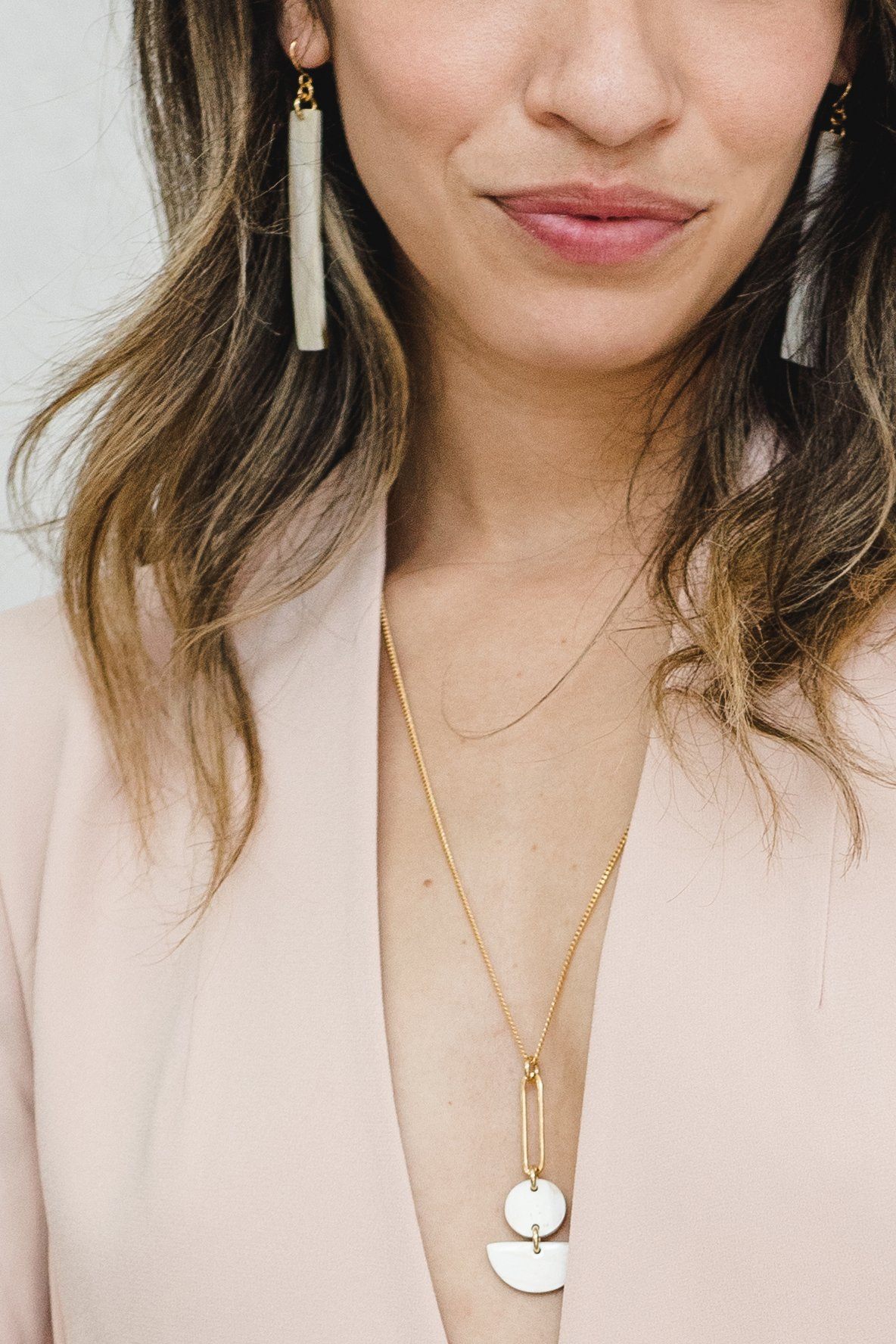Close-up of a person wearing a gold necklace with a pendant and long earrings.