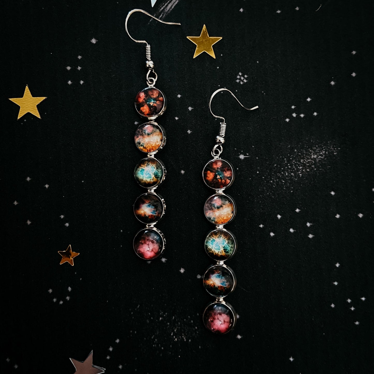 Pair of earrings with celestial design on a black background with star decorations