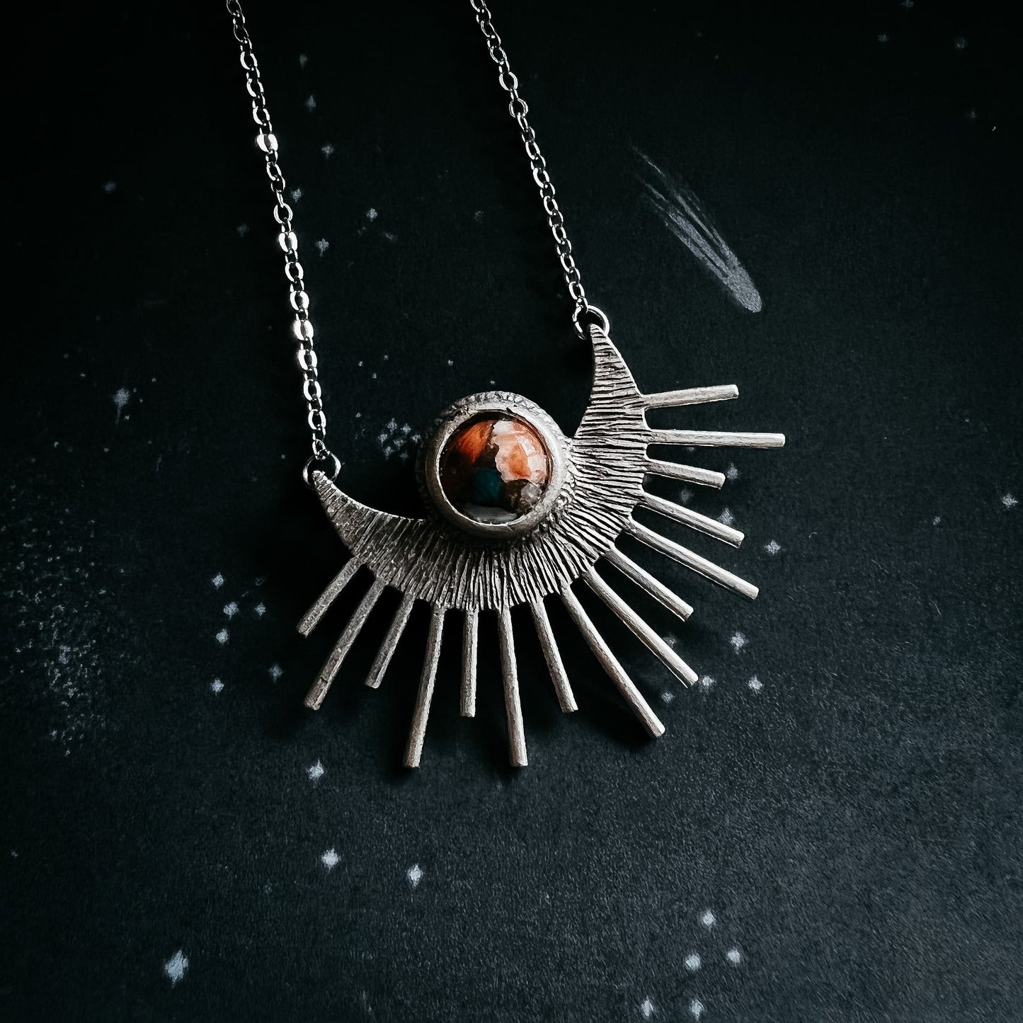 Silver sun-shaped pendant necklace with a central gemstone on a dark background
