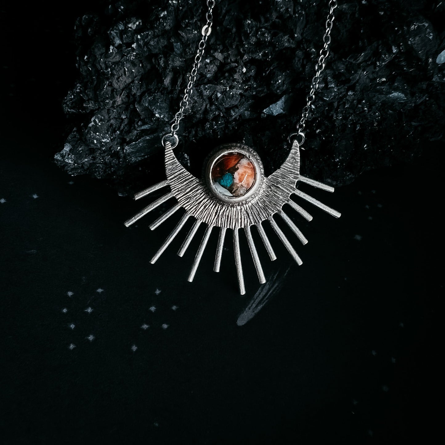Silver necklace with a sun-like pendant on a dark background