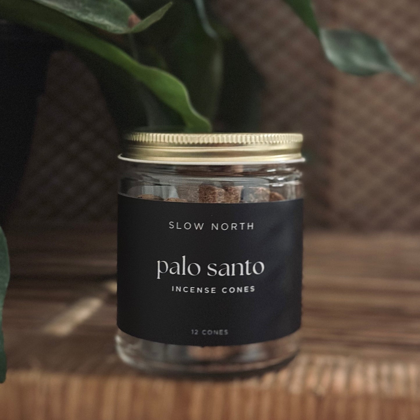 Jar of Slow North Palo Santo Incense Cones on a wooden surface with green leaves in the background