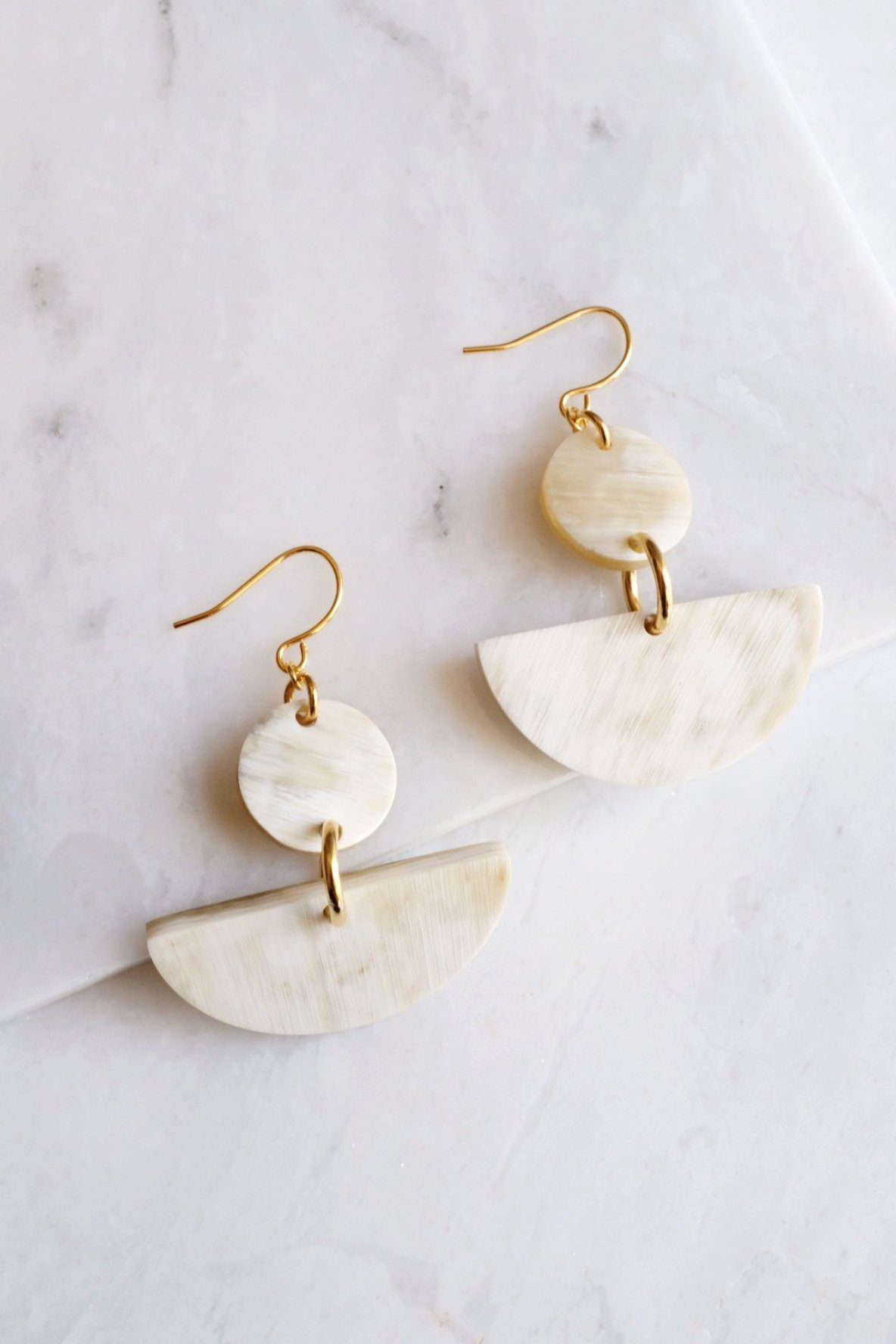 Pair of gold and beige half-circle earrings on a marble surface