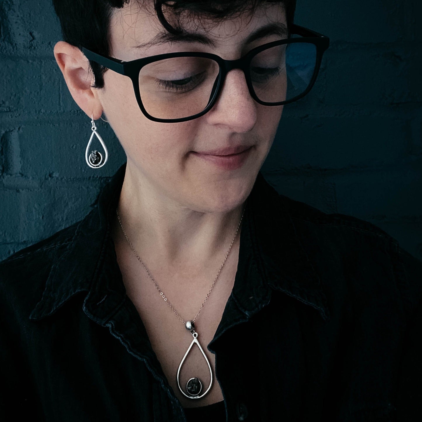 Person wearing black glasses and a black shirt with a dark background