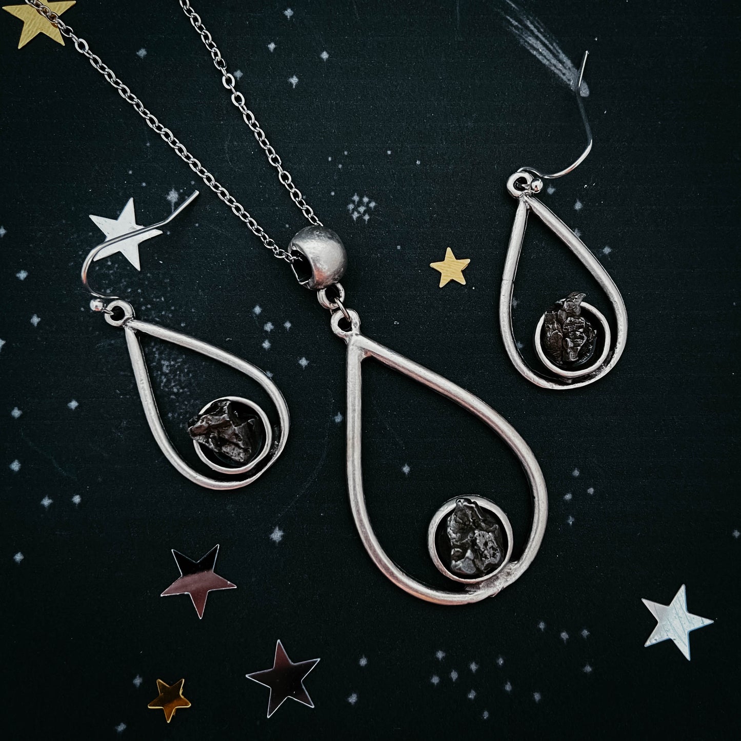 Silver teardrop-shaped jewelry set with star decorations on a dark background