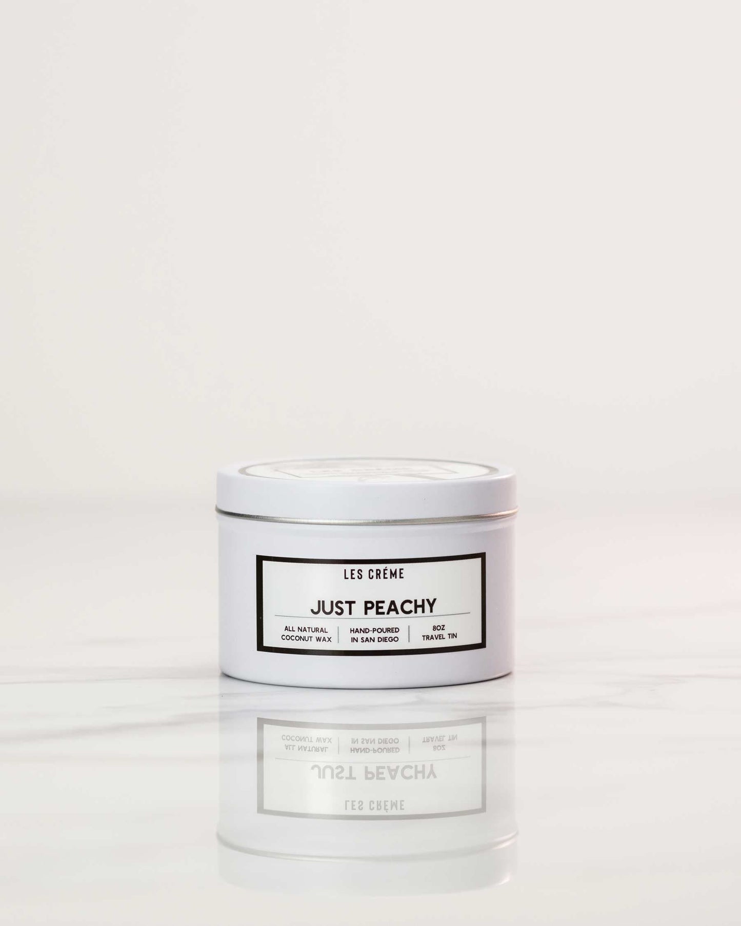 White candle jar labeled 'Just Peachy' by Les Creme on a white background