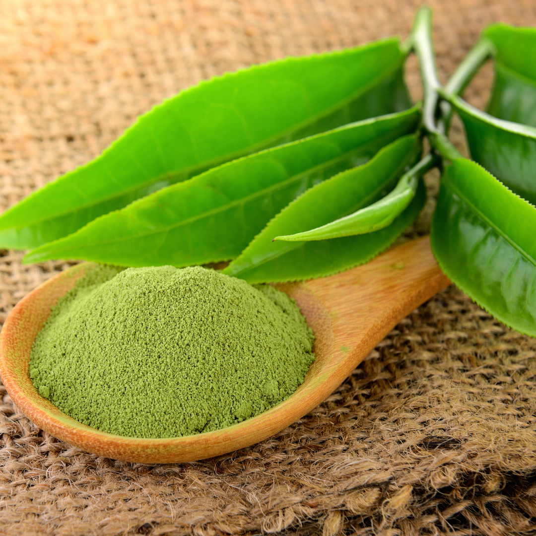 Wooden spoon filled with green powder next to green leaves on a burlap background