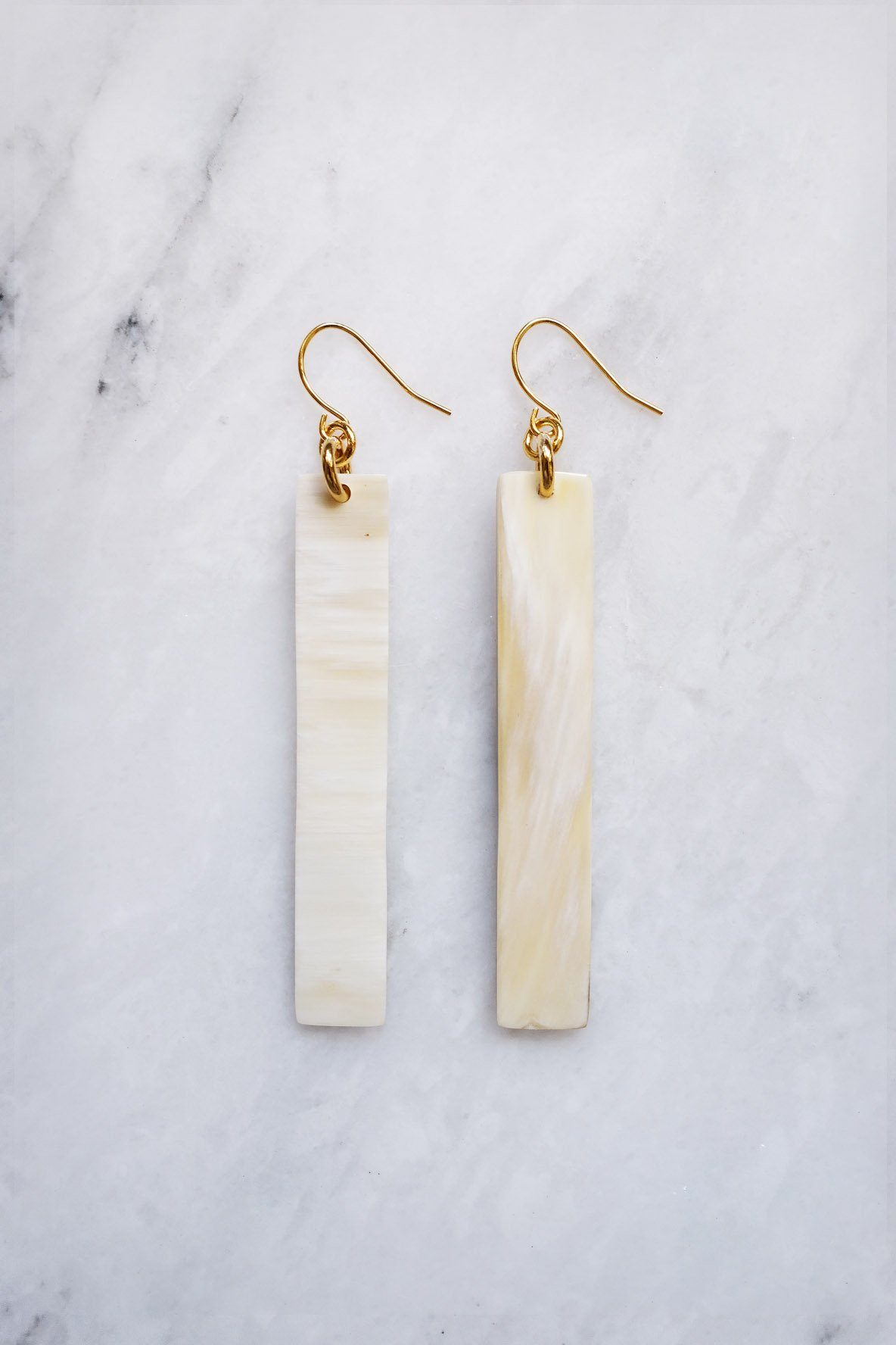 Pair of gold earrings with long, thin, beige stones on a marble background