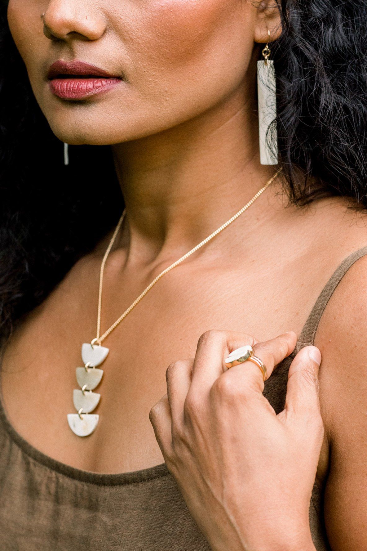 Woman wearing a gold necklace with layered pendants and a ring on her finger.
