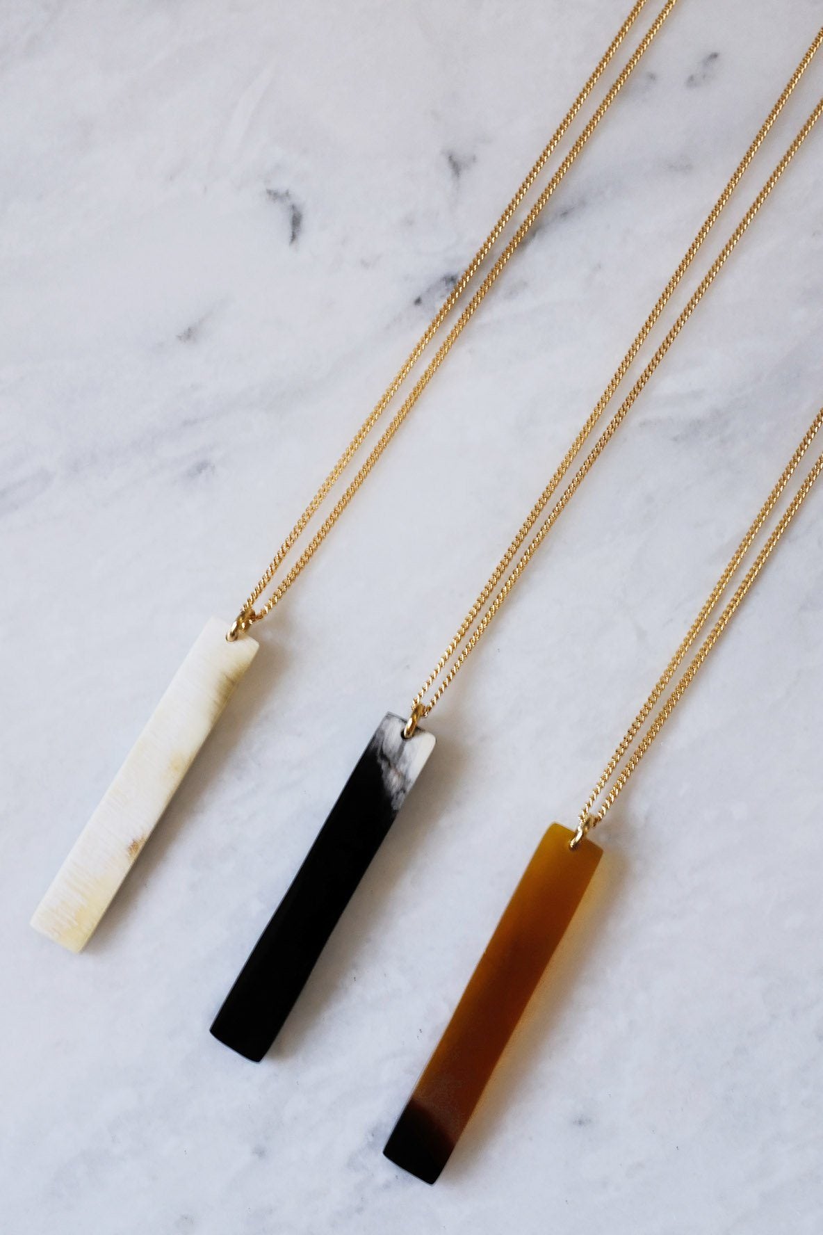 Three necklaces with different colored pendants on a marble surface