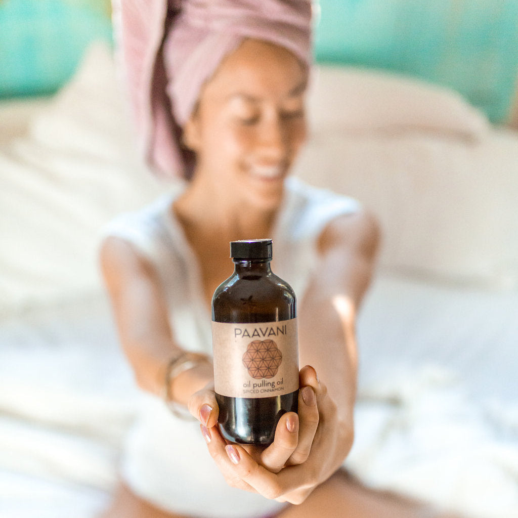 Woman holding a bottle of Paavani Ayurved oil with a blurred background