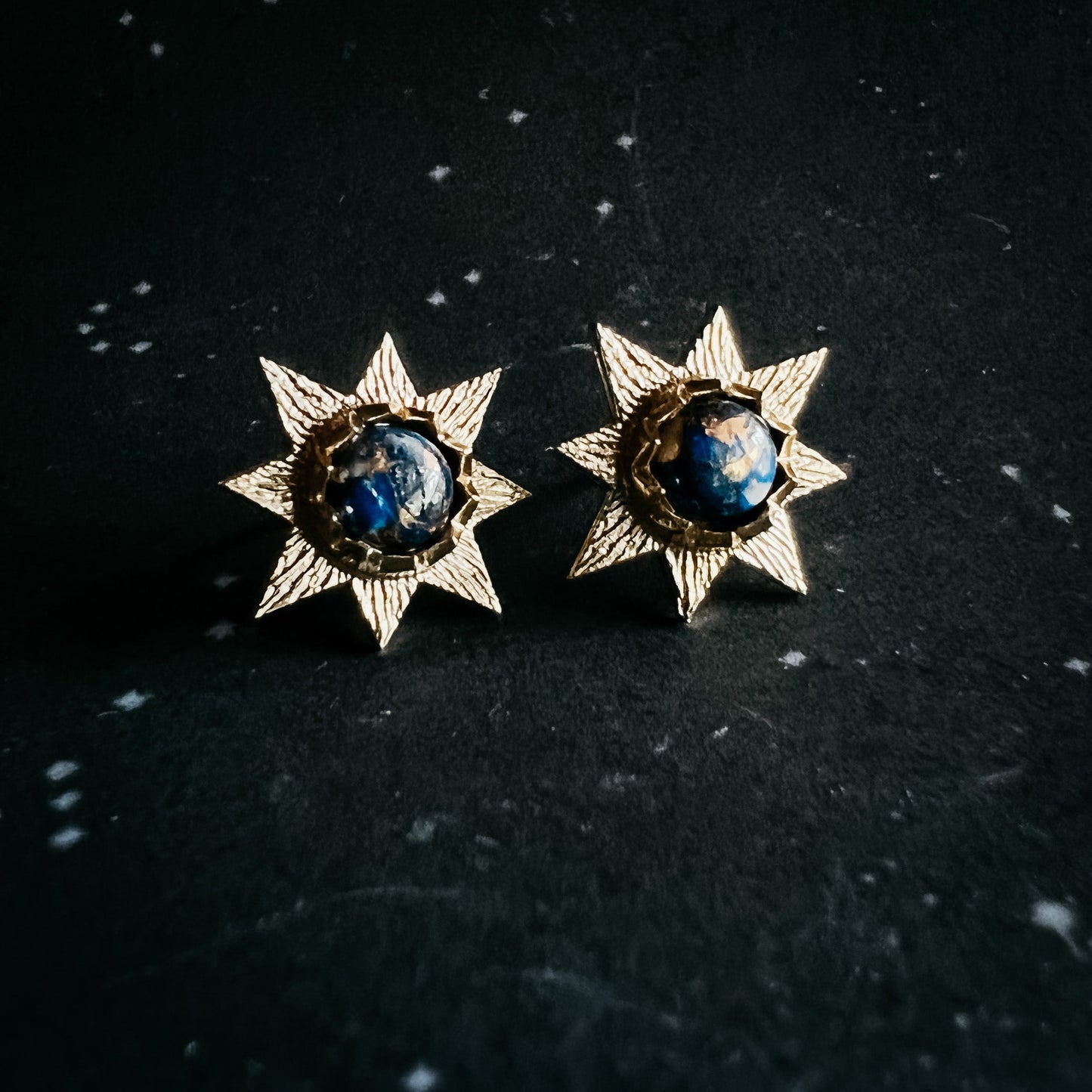 Pair of star-shaped earrings with blue gemstones on a dark background