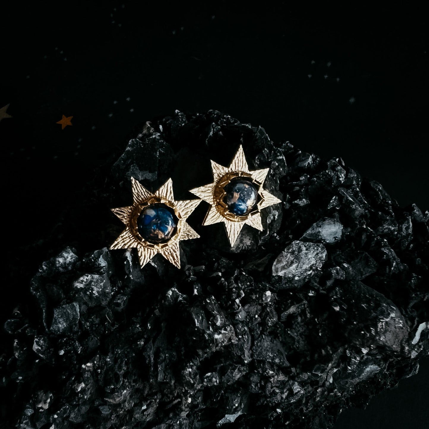 Star-shaped earrings with blue gemstones on a dark textured surface