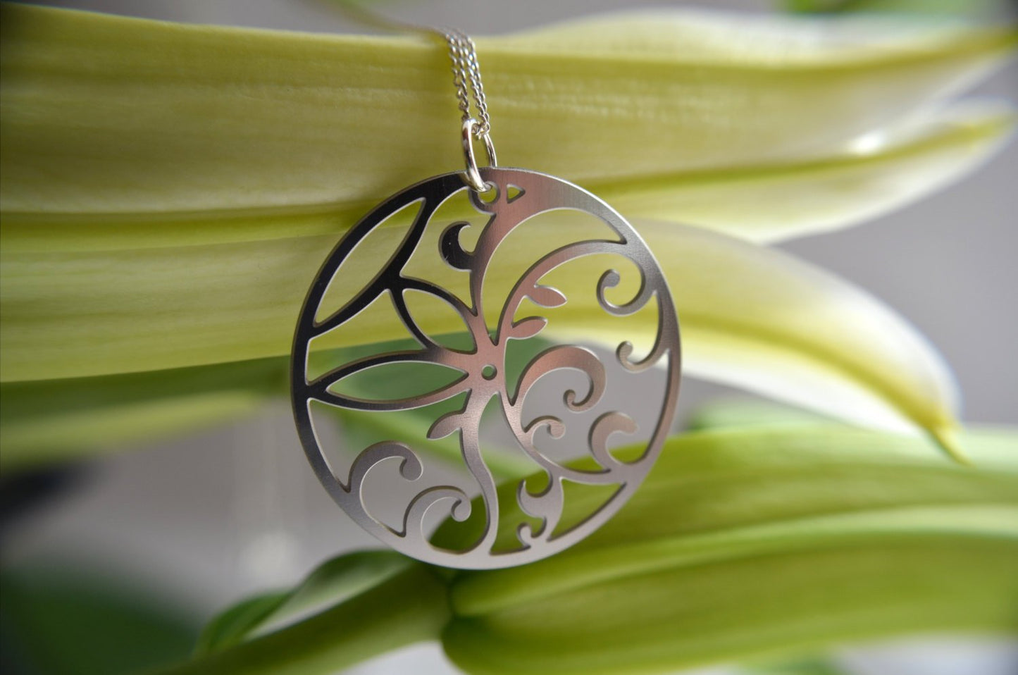 Silver butterfly pendant necklace on a green leaf