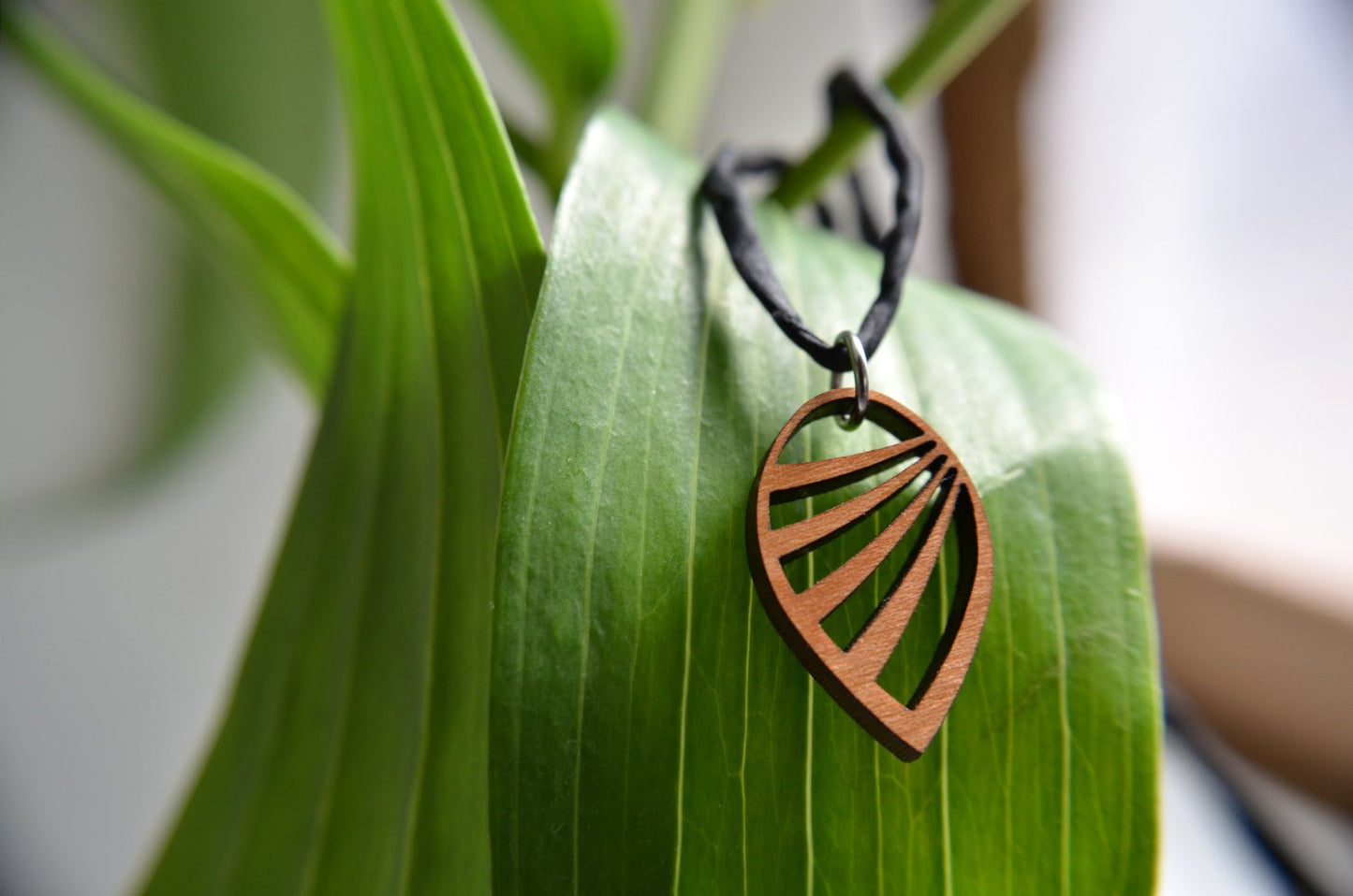 Copper leaf-shaped pendant on a black cord hanging on a green leaf
