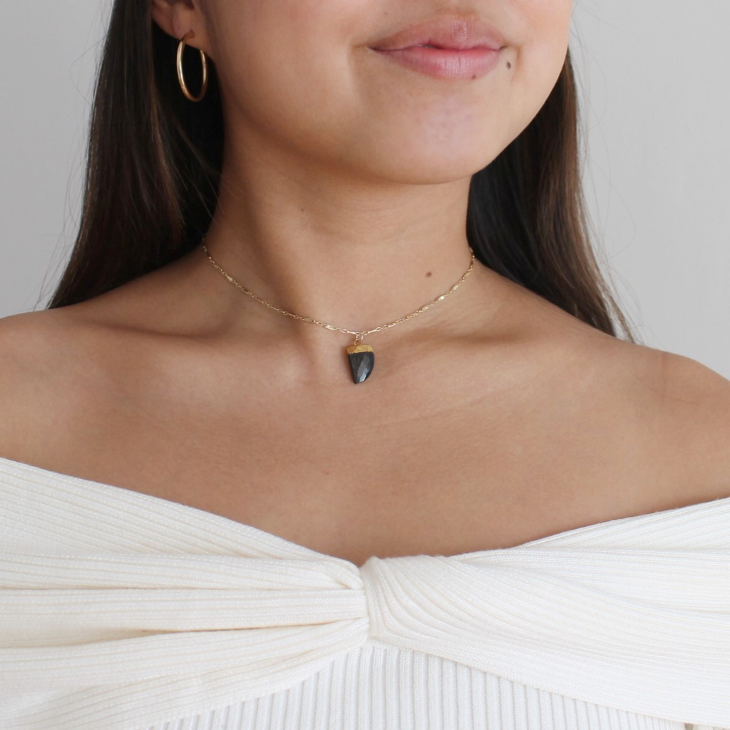 Woman wearing a delicate necklace with a black pendant on a plain background
