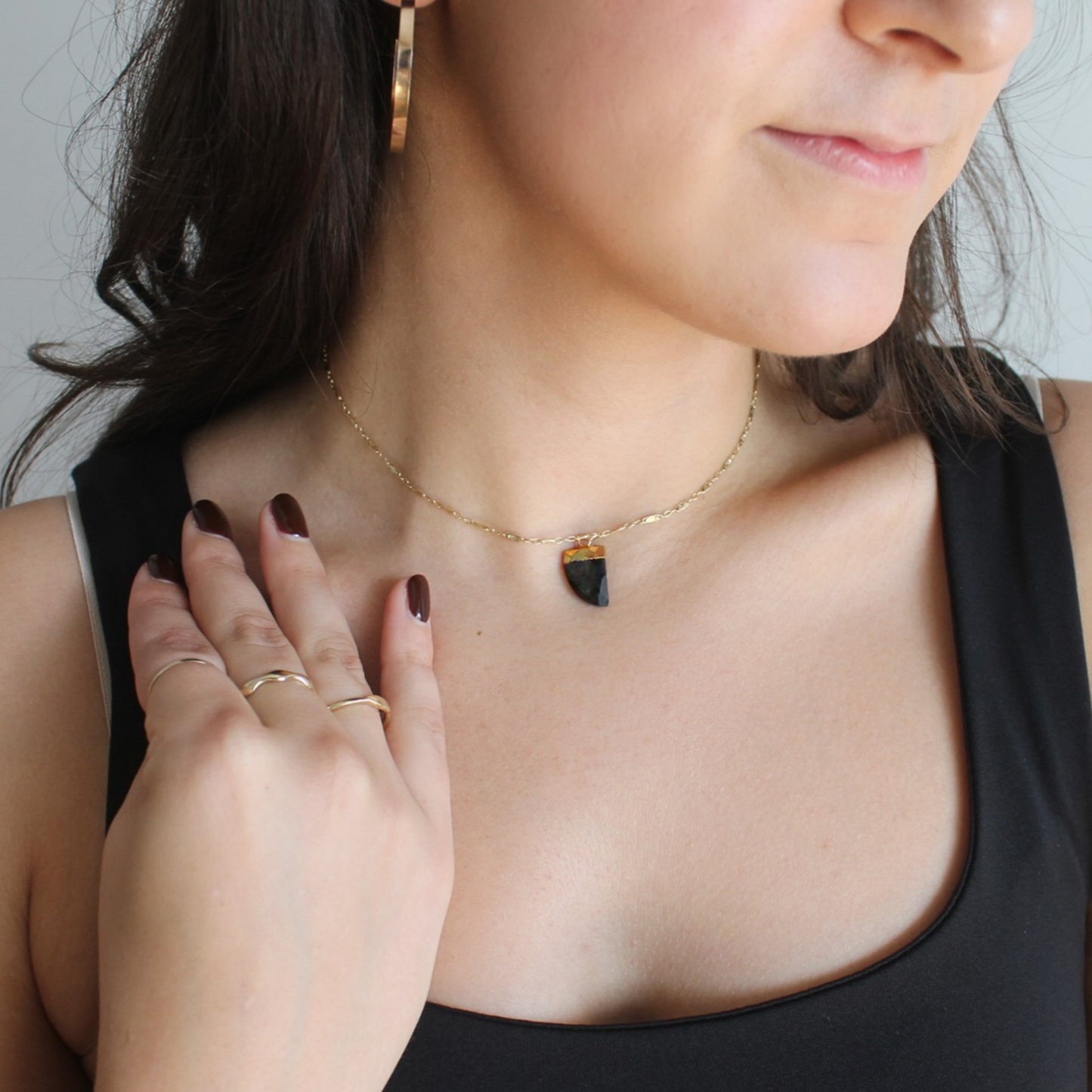 Woman wearing a gold necklace with a black pendant, holding her hand near her neck.