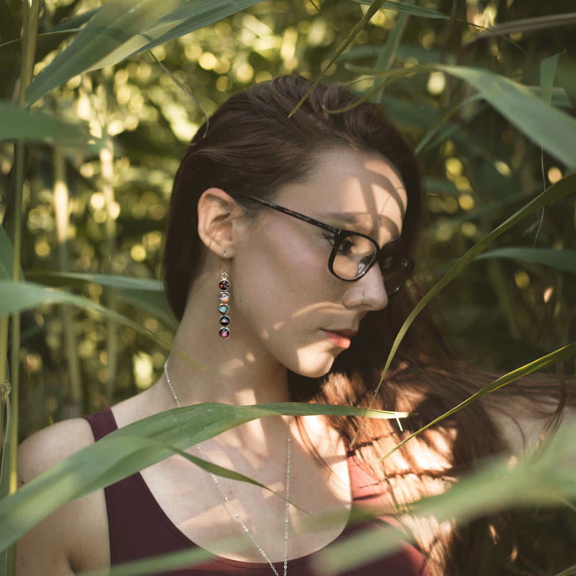 Woman with glasses and earrings standing among green plants