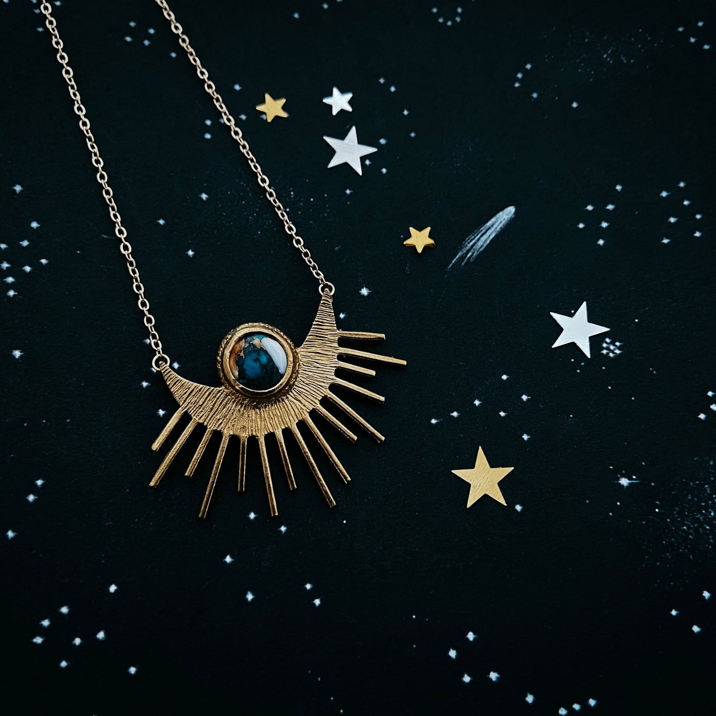 Gold necklace with a sun-shaped pendant on a dark background with star illustrations