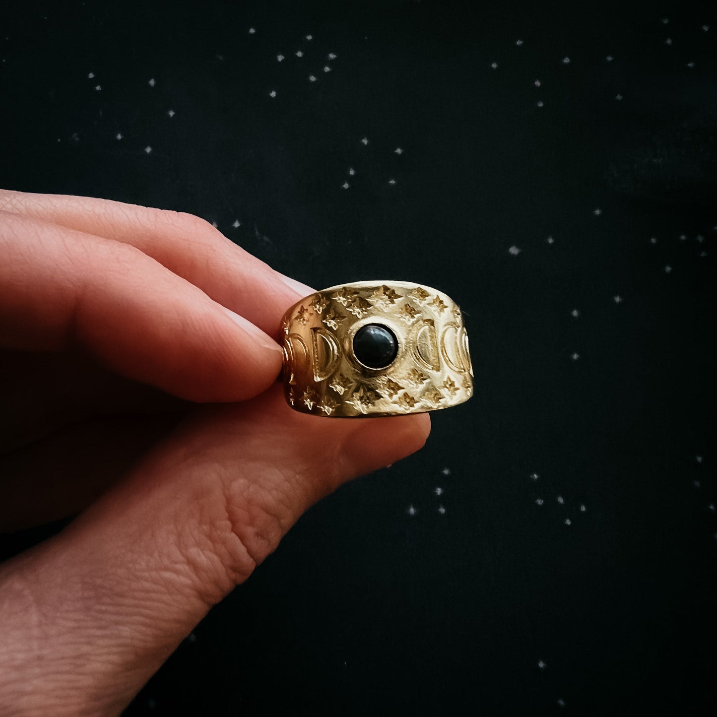 Gold ring with a black gemstone held by a hand against a dark background