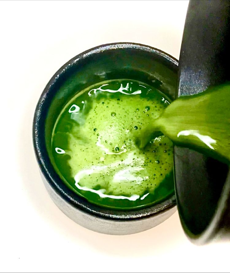 Green liquid being poured into a black cup on a white background