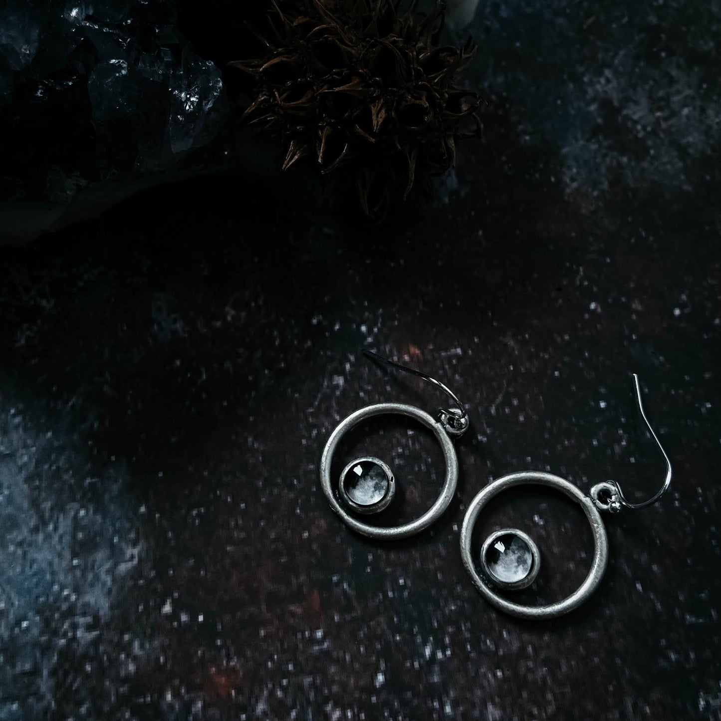 Pair of silver earrings with gemstones on a dark textured surface