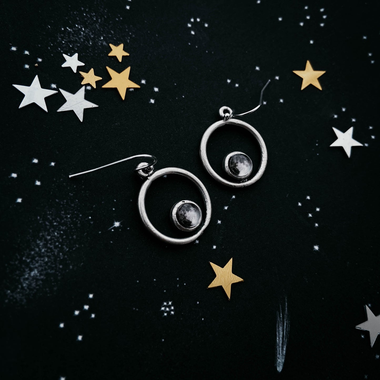 Silver earrings with circular designs on a black background with star decorations