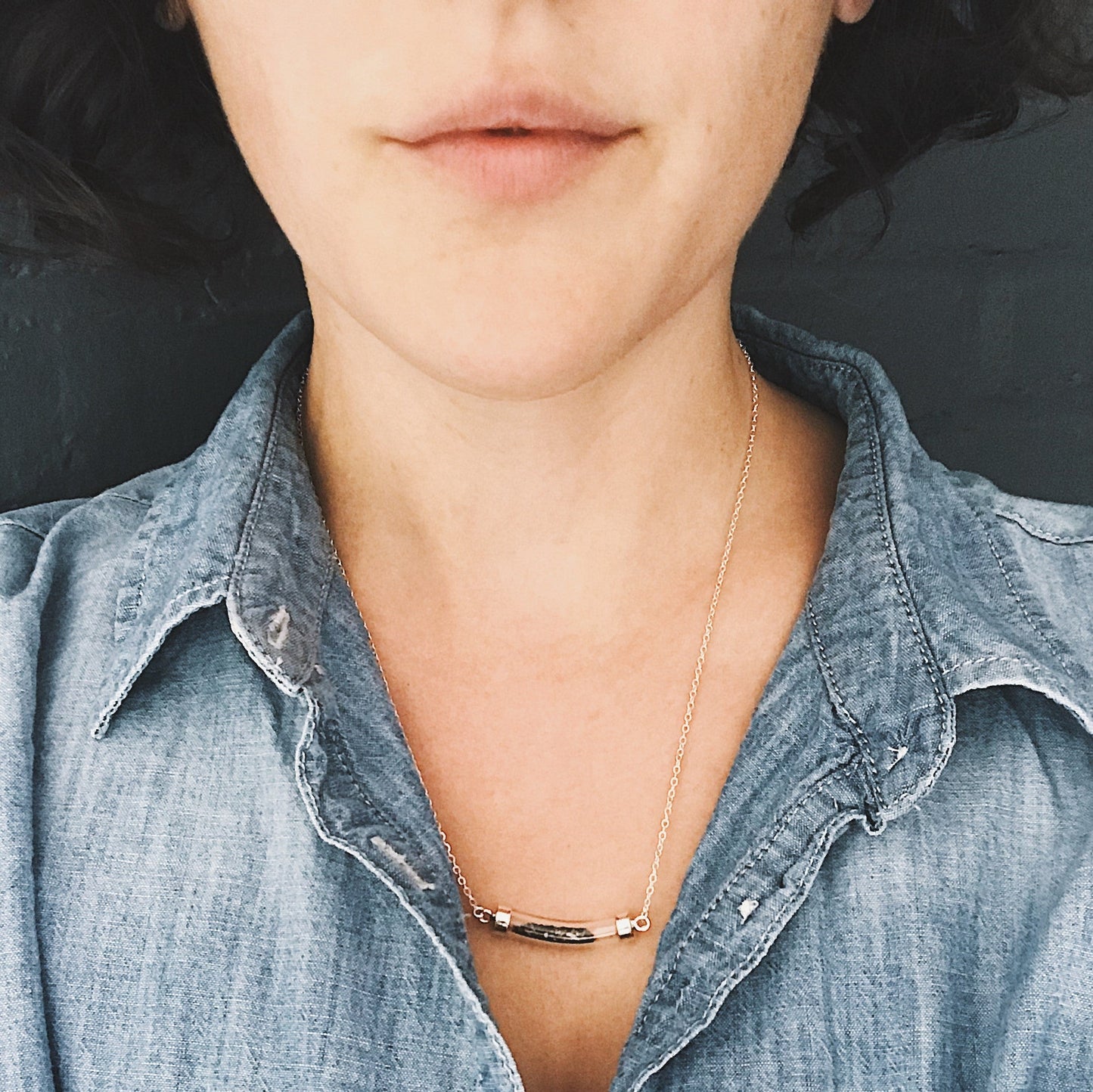 Person wearing a gold necklace with a minimalistic design, dressed in a denim shirt.