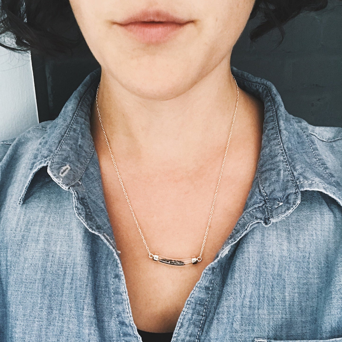 Person wearing a gold necklace with a minimalistic design, wearing a denim shirt.