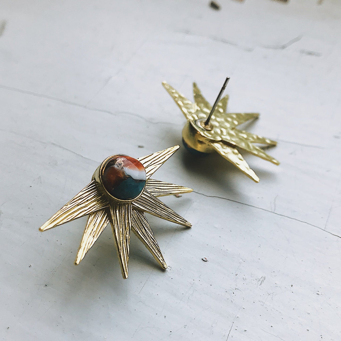 Gold star-shaped earrings with a central stone on a light surface