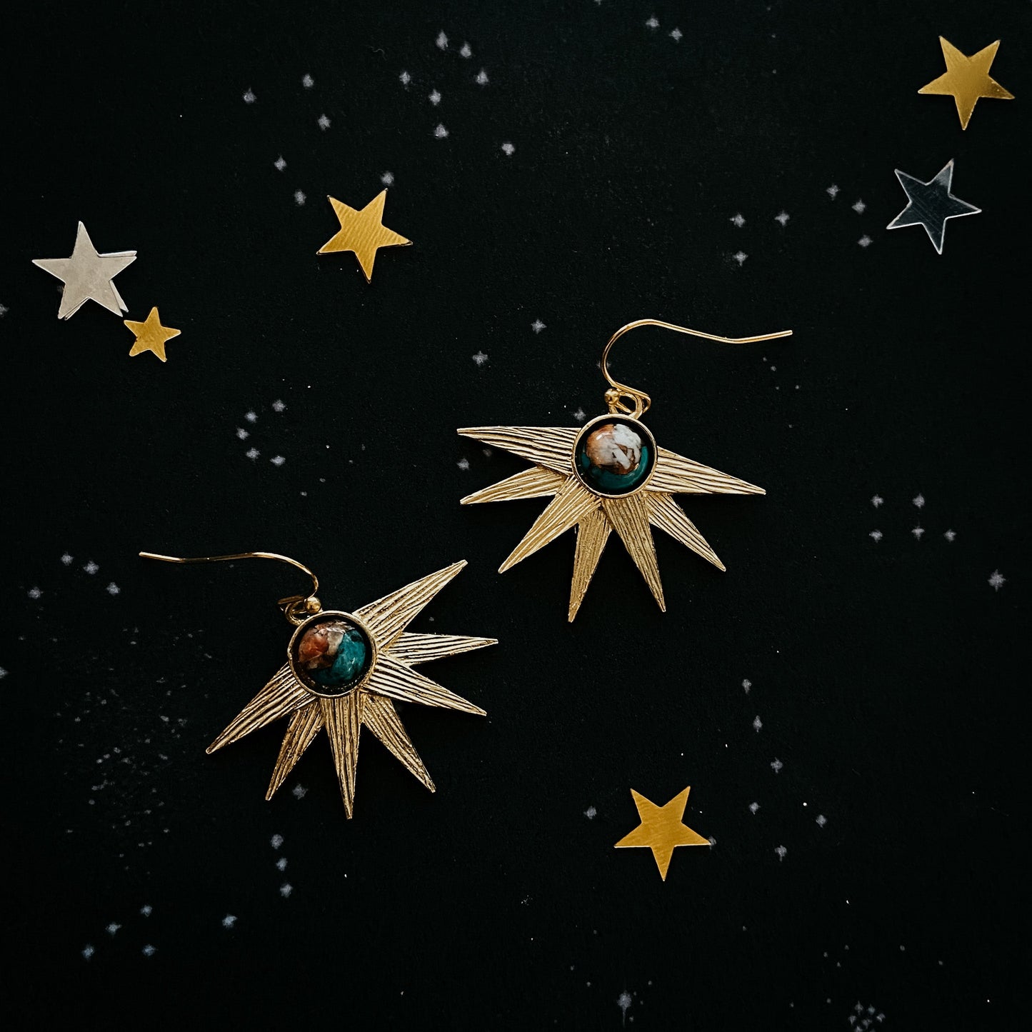 Star-shaped earrings with gemstones on a black background with star illustrations