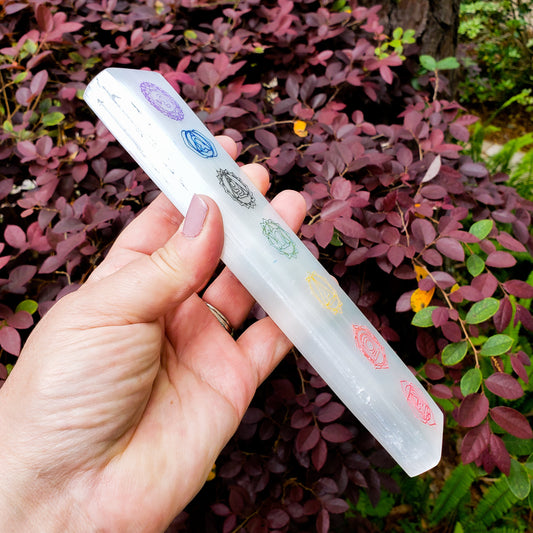 Hand holding a crystal wand with symbols against a natural background