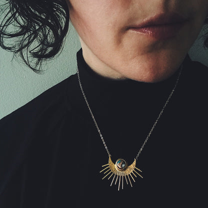 Person wearing a necklace with a sun and moon pendant against a green background