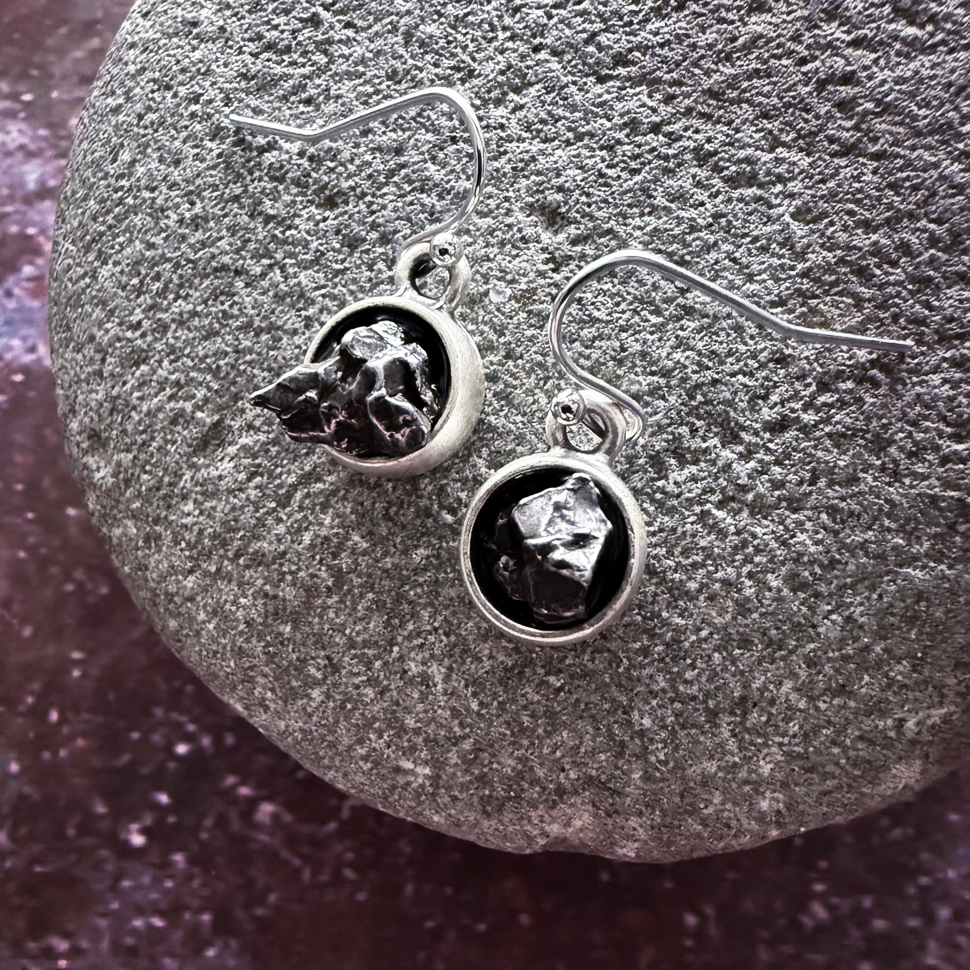 Silver earrings with dark gemstones on a textured stone surface