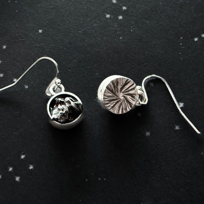 Two silver earrings on a black background