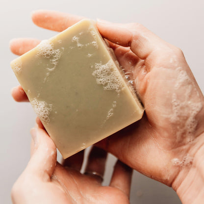 Hand holding a bar of soap with lather on a neutral background