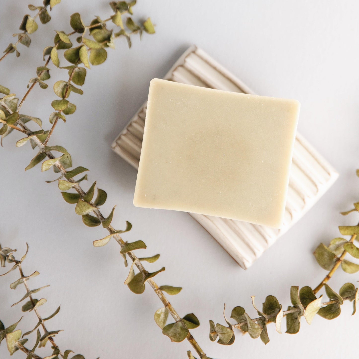 Bar of soap on a white surface with eucalyptus leaves