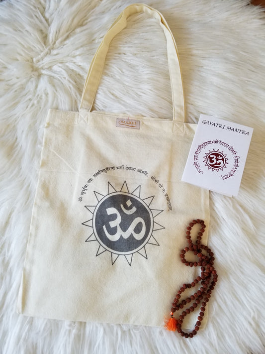 Beige tote bag with Om symbol, mala beads, and a card on a fluffy white surface