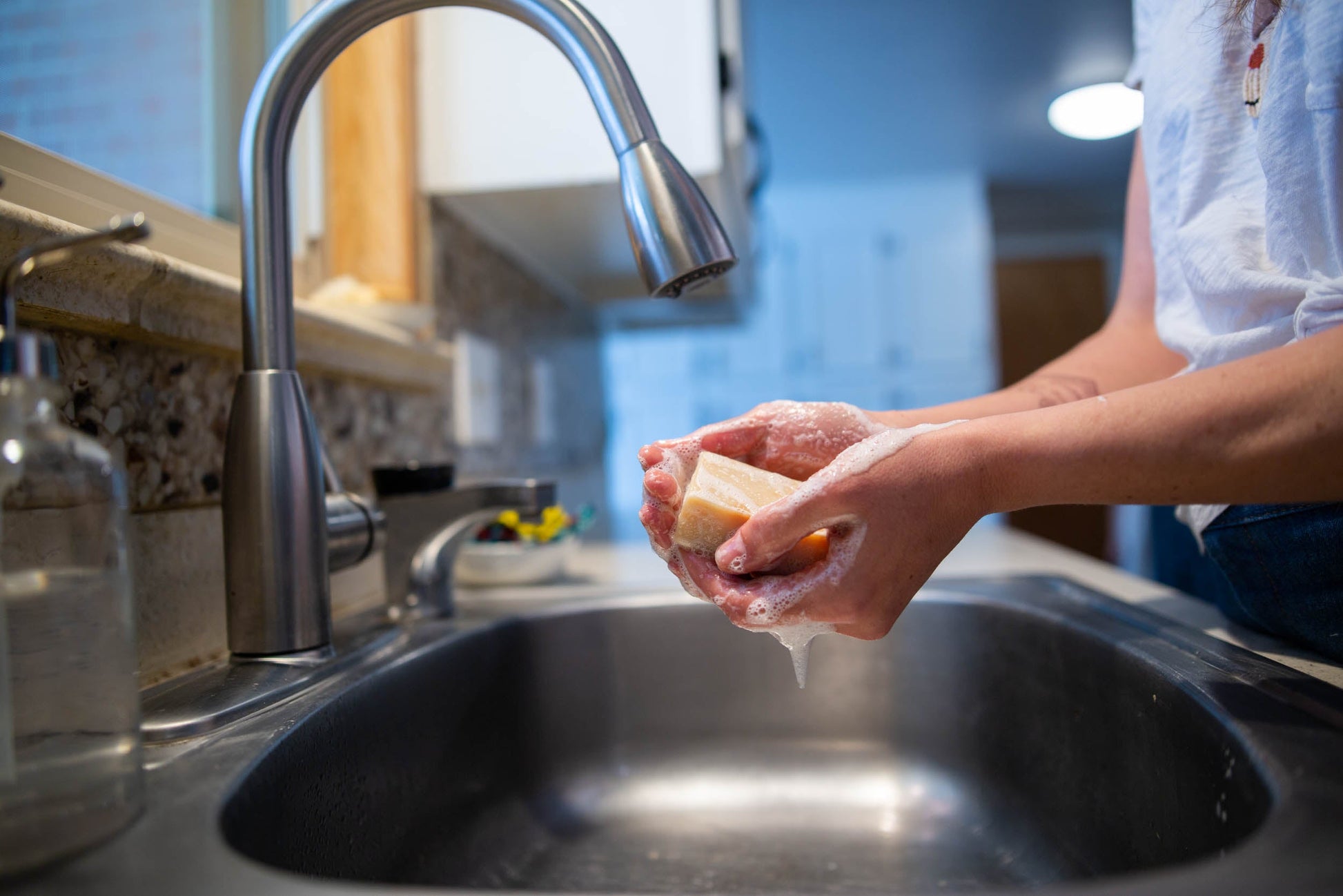 Person washing hands with soap under a faucet in a kitchen sink.