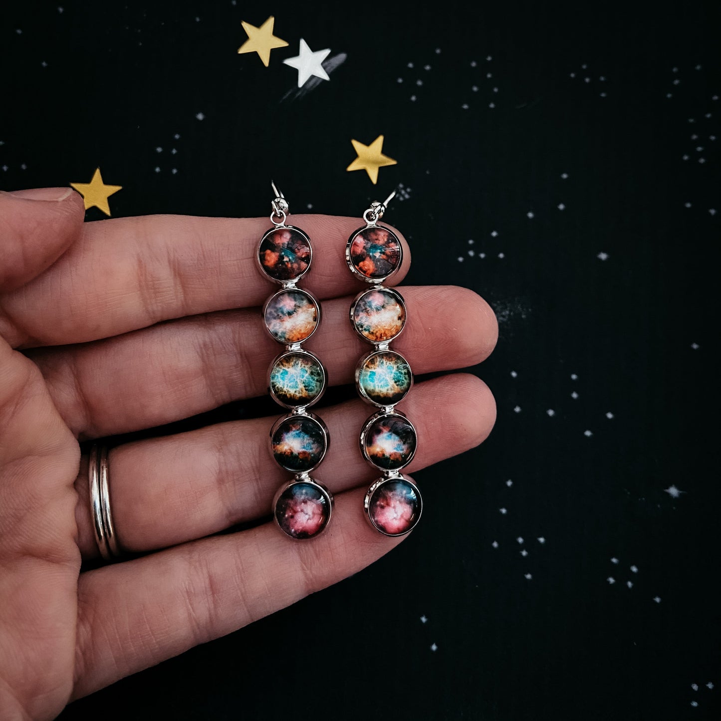 Pair of earrings with celestial design held in a hand against a starry background