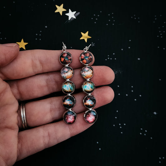 Pair of earrings with celestial design held in a hand against a starry background