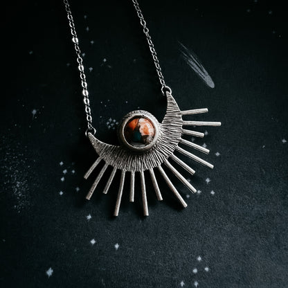 Silver sun-shaped pendant necklace with a central gemstone on a dark background