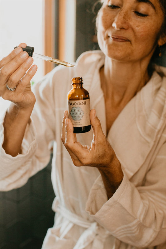 Woman applying a skincare product from a bottle labeled 'Nava' in a bathroom setting.