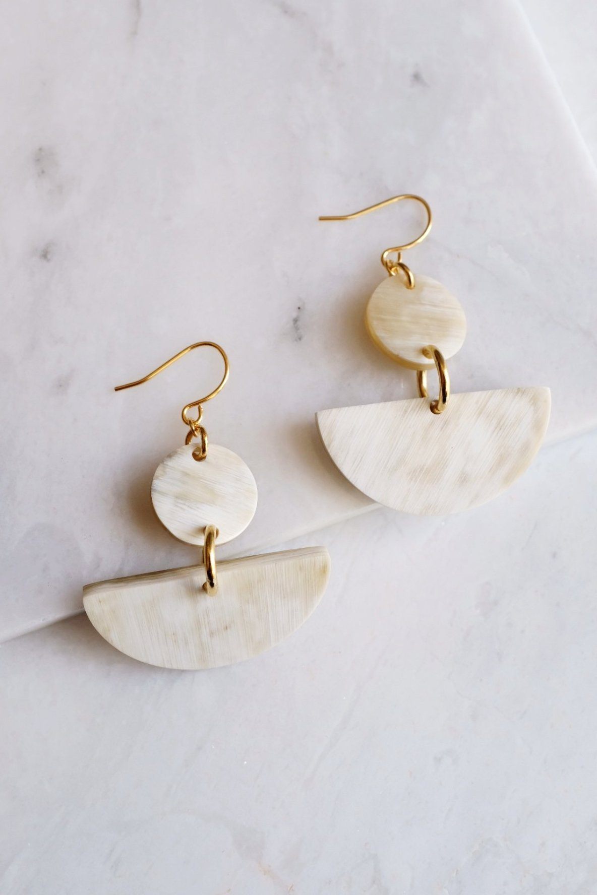 Pair of gold and beige half-circle earrings on a marble surface